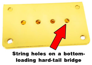 Bottom-loading hard-tail bridges have string holes in the base plate, as shown here. Strings are fed up through the body of the instrument. This gold 4-string hard-tail bridge is available from CBGitty.com.